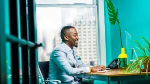 Confident businessman in modern office working on laptop with city view., tags: african - pexel