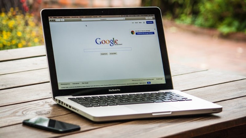 A MacBook Pro displaying Google Search on a wooden table outdoors, next to a smartphone. - A MacBook Pro displaying Google Search on a wooden table outdoors, next to a smartphone., tags: campaigns - pexel