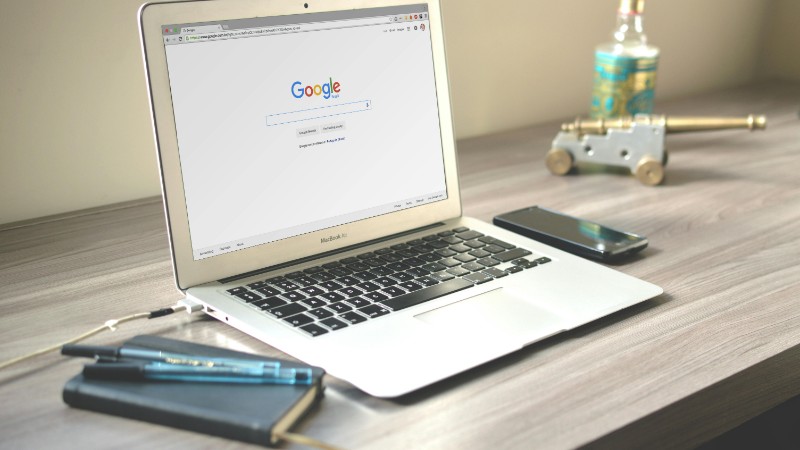 A neat workspace featuring a laptop displaying Google search, a smartphone, and a notebook on a wooden desk., tags: gambling - pexel