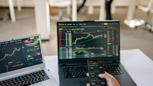 A professional tracks stock market trends using two laptops and a smartphone, showcasing digital finance tools., tags: fintech ppc - pexel