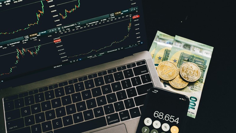 A laptop displaying stock charts with Bitcoin, Euros, and a cellphone calculator, showcasing financial analysis., tags: fintech advertising - pexel