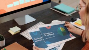 A businesswoman reviews marketing documents with charts at her desk, featuring a computer and office supplies., tags: ads - pexel
