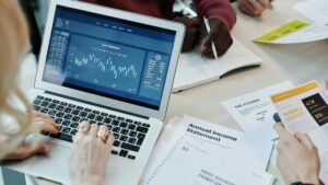 Business professionals analyzing financial data on a laptop during a meeting. Charts and reports visible., tags: paid ads - pexel